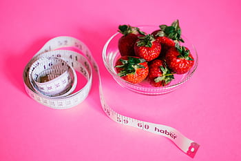 A glass bowl of fresh strawberries paired with a pink measuring tape symbolizes healthy eating. HD wallpaper