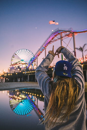 Back view of a woman enjoying Santa Monica Pier amusement park at twilight, reflecting vibrant lights. HD phone wallpaper