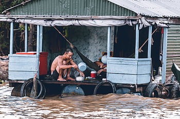 A man sits on a flooded wooden houseboat during a heavy flood. HD wallpaper