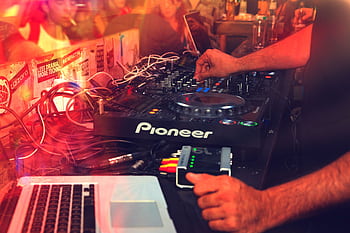 DJ operating a mixer during a lively nightclub party with vibrant lights. HD wallpaper