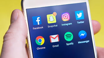 A person's hand holding a smart displaying social media and communication apps. HD wallpaper