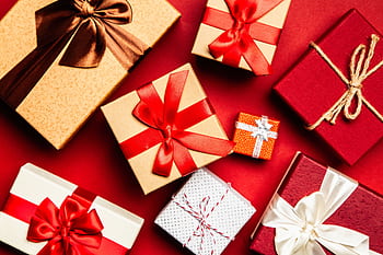 Top view of beautifully wrapped holiday gifts with red and brown ribbons on a vibrant red background. HD wallpaper
