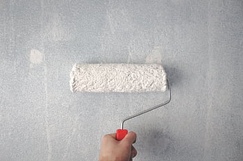 A person's hand using a paint roller to apply white paint on a wall. HD wallpaper