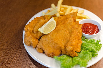 Delicious schnitzel served with fries, lettuce, lemon, and ketchup on a wooden table. HD wallpaper
