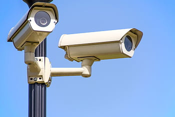 Outdoor security cameras mounted on a pole against a clear blue sky, ensuring vigilant surveillance. HD wallpaper