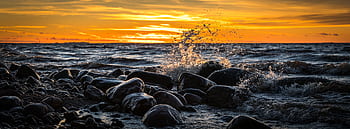 Captivating sunset with waves crashing over rocks on a que seashore. HD wallpaper