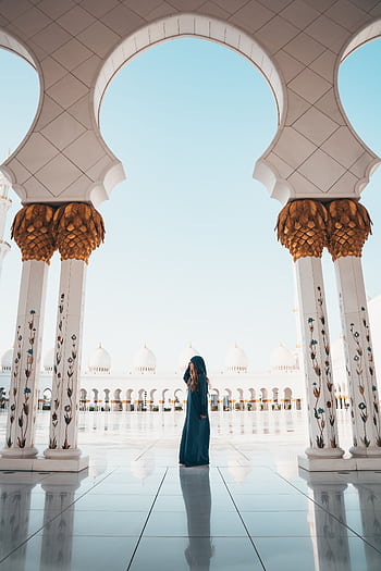 A person in traditional attire standing among columns of the Sheikh Zayed Mosque in Abu Dhabi. HD phone wallpaper