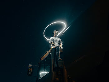 A man sits on a truck, surrounded by a light halo under a starry sky. HD wallpaper