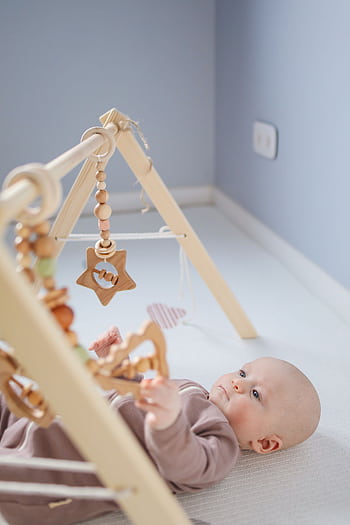 A serene baby lying in a room playing with a wooden toy, creating a peaceful and cozy atmosphere. HD phone wallpaper