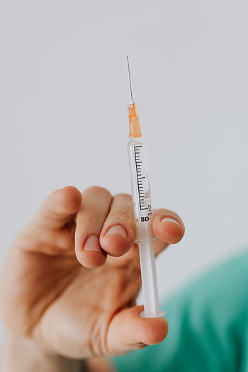 Detailed close-up shot of a hand holding a medical syringe against a neutral background. HD phone wallpaper