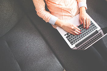 A woman typing on a laptop, sitting on a sofa in casual attire, viewed from above. HD wallpaper
