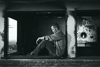 A young man sits pensively in a derelict building, embodying solitude and contemplation. HD wallpaper