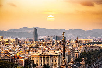 A stunning sunset view of the Barcelona skyline showcasing iconic landmarks and a warm, golden hour glow. HD wallpaper