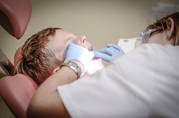 A young boy receiving a dental examination by a professional dentist in a clinic setting. HD wallpaper