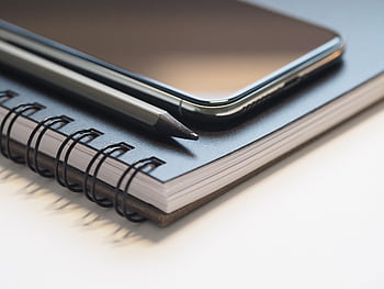 Close-up of a spiral notebook, smart, and pencil on a desk, highlighting modern workspace essentials. HD wallpaper