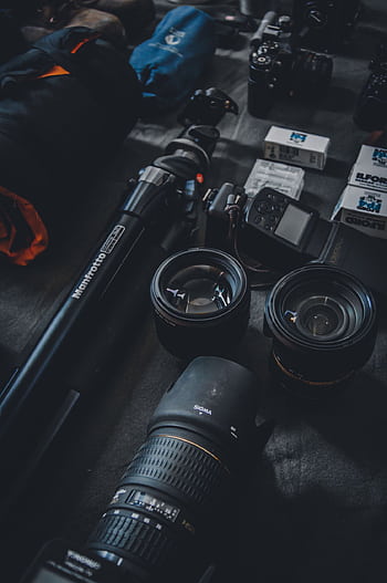Close-up of a graphy setup featuring camera lenses, tripod, and film rolls for professional use. HD phone wallpaper