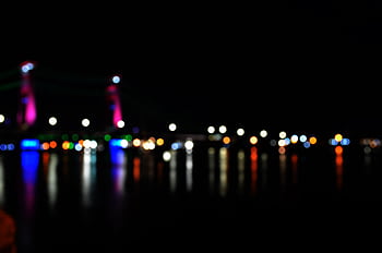 Blurred view of Ampera Bridge lights reflecting in water, creating bokeh effects. HD wallpaper