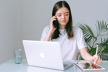 A young woman multitasking with a , laptop, and tablet in a bright home office setting. HD wallpaper