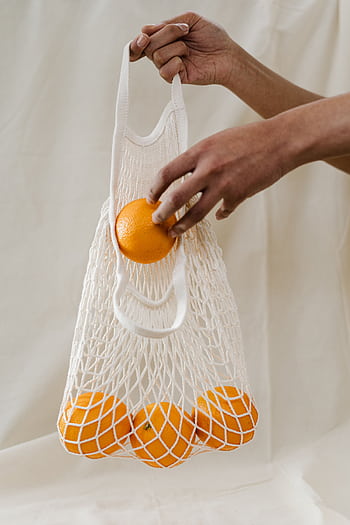 Hand holding a reusable mesh bag filled with fresh oranges, promoting sustainability and zero waste shopping. HD phone wallpaper