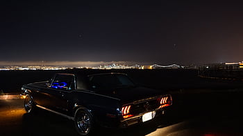 Iconic Mustang parked by the waterfront with city skyline and bridge illuminated at night. HD wallpaper