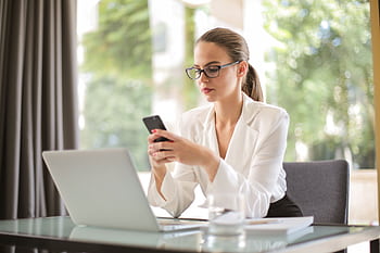 Confident businesswoman in eyeglasses checking smart at the office desk with a laptop. HD wallpaper
