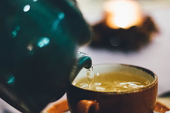 Warm close-up of tea being poured into a teacup with blurred background ambiance. HD wallpaper