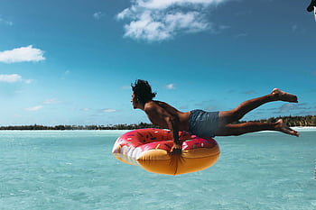 Man jumping into turquoise water with a donut float in French Polynesia. HD wallpaper