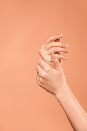 Close-up of soft, smooth hands with elegant pose on a peach background, showcasing skincare beauty. HD phone wallpaper