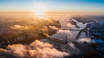 Stunning aerial sunrise view over a city with bridges and a river enveloped in cloud cover. HD wallpaper