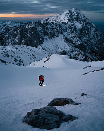 Lone mountaineer trekking up a snow-covered peak at sunrise in Slovenia. HD phone wallpaper