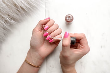 Close-up of a woman applying glitter nail polish to manicured pink fingernails. HD wallpaper