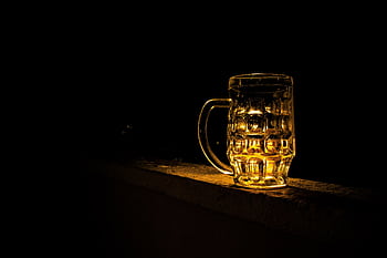 A glass beer mug illuminated against a dark background, creating a moody atmosphere. HD wallpaper
