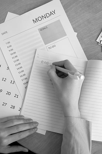 A monochrome of a person planning their week with a notebook, calendar, and goals list. HD phone wallpaper