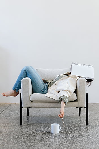 Tired woman in casual attire falls asleep on sofa with a notebook on face and pen in hand. HD phone wallpaper