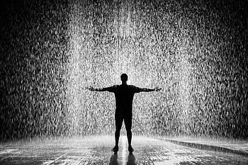 A person joyfully standing in the rain with arms wide open in a dramatic black and white scene. HD wallpaper