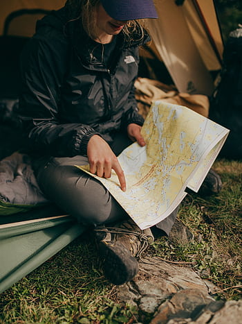 A woman sits in a tent studying a map during a camping trip in the wilderness. HD phone wallpaper