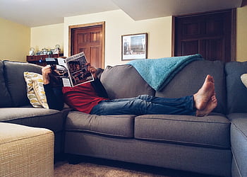 Person relaxing on a comfortable sofa reading a magazine in a cozy living room. HD wallpaper