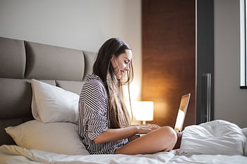 Young woman enjoying leisure time on her laptop in a comfortable bedroom environment. HD wallpaper
