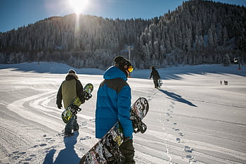 Group of snowboarders walking up a snowy ski slope during a sunny winter day in the mountains. HD wallpaper