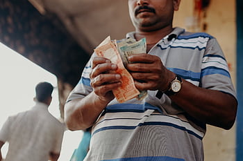 Man in Indian market counting rupee notes, showcasing daily street commerce. HD wallpaper