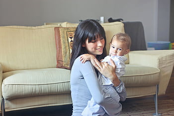 A mother lovingly embraces her baby indoors on a comfortable sofa capturing warmth and togetherness. HD wallpaper