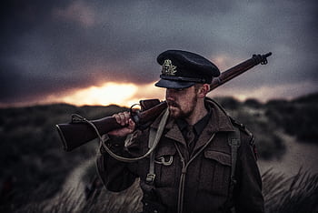 A soldier in uniform holding a rifle against a dramatic sunset background. HD wallpaper