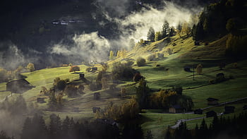 Scenic view of a misty hillside landscape with scattered cabins in autumn light. HD wallpaper