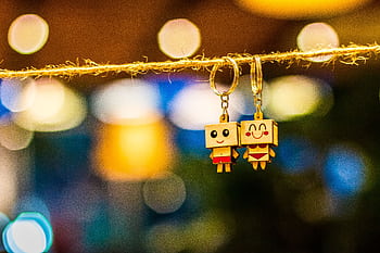 Charming wooden cartoon keychain dolls hanging with vibrant bokeh lights in the background, creating a playful and colorful ambiance. HD wallpaper
