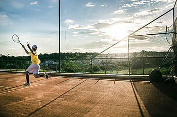 Capture the intensity of a young athlete performing on an outdoor tennis court at sunset. HD wallpaper