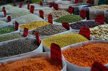 Bags of vibrant grains and spices on display in a bustling market setting. HD wallpaper