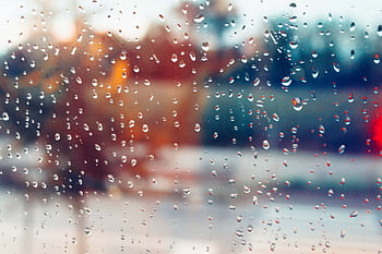 Rain droplets on window creating a blurry, colorful bokeh effect with a moody ambiance. HD wallpaper