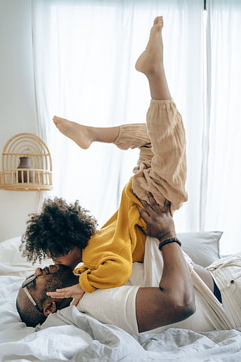 A joyful moment of a father and child playing on bed indoors, capturing family love. HD phone wallpaper