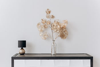 A stylish minimalist interior with a floral arrangement and a sleek lamp on a wooden table. HD wallpaper