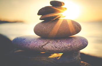 Stacked stones by the ocean create a tranquil scene during a beautiful sunset. HD wallpaper